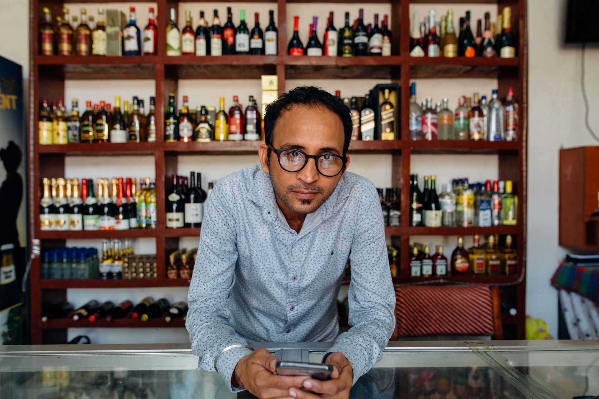 Liquor store clerk at the checkout counter with shelves of wine and spirits behind