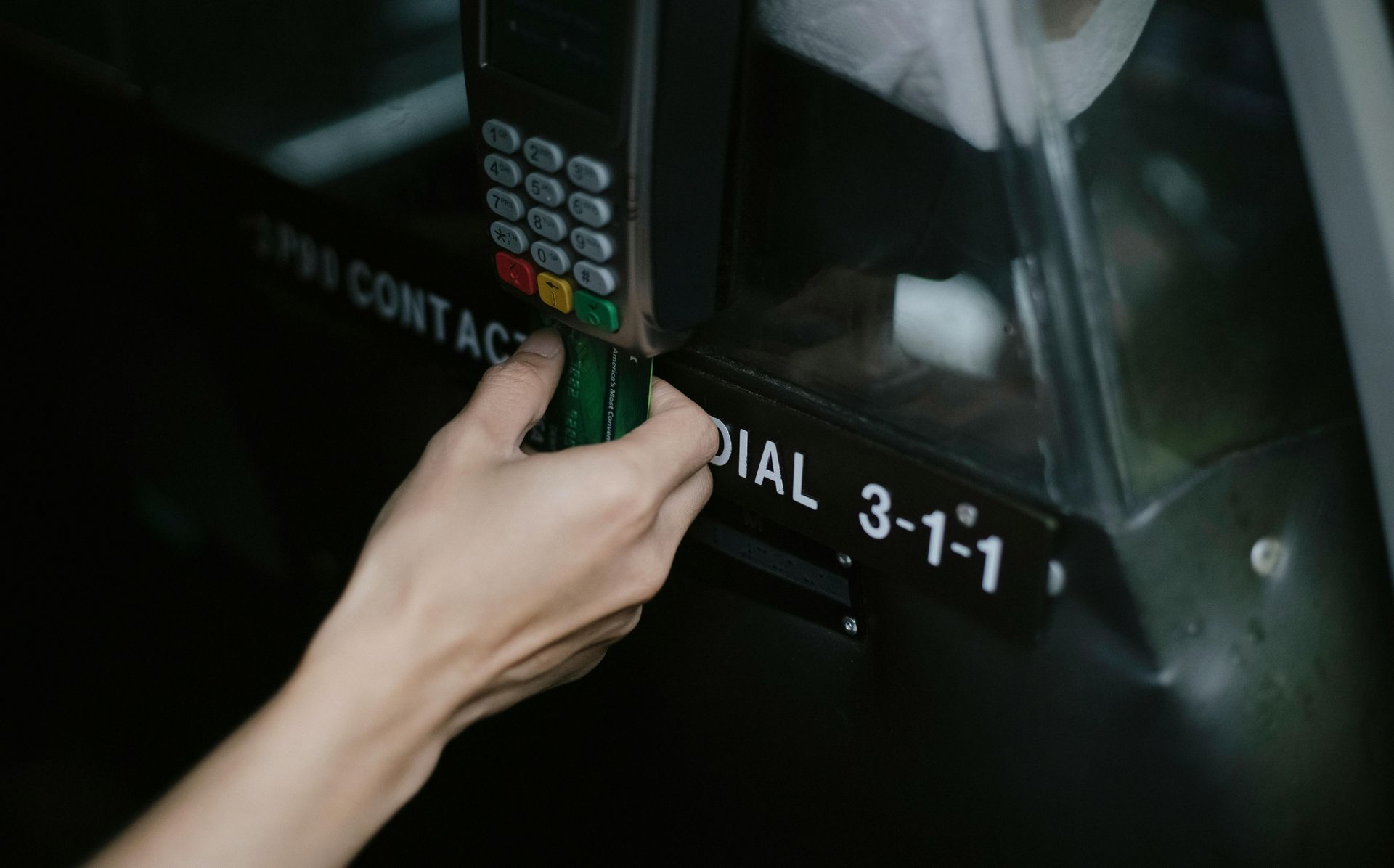 Hand holding a card to a contactless reader near a black sign reading “CONTACTLESS DIAL 3-1-1”