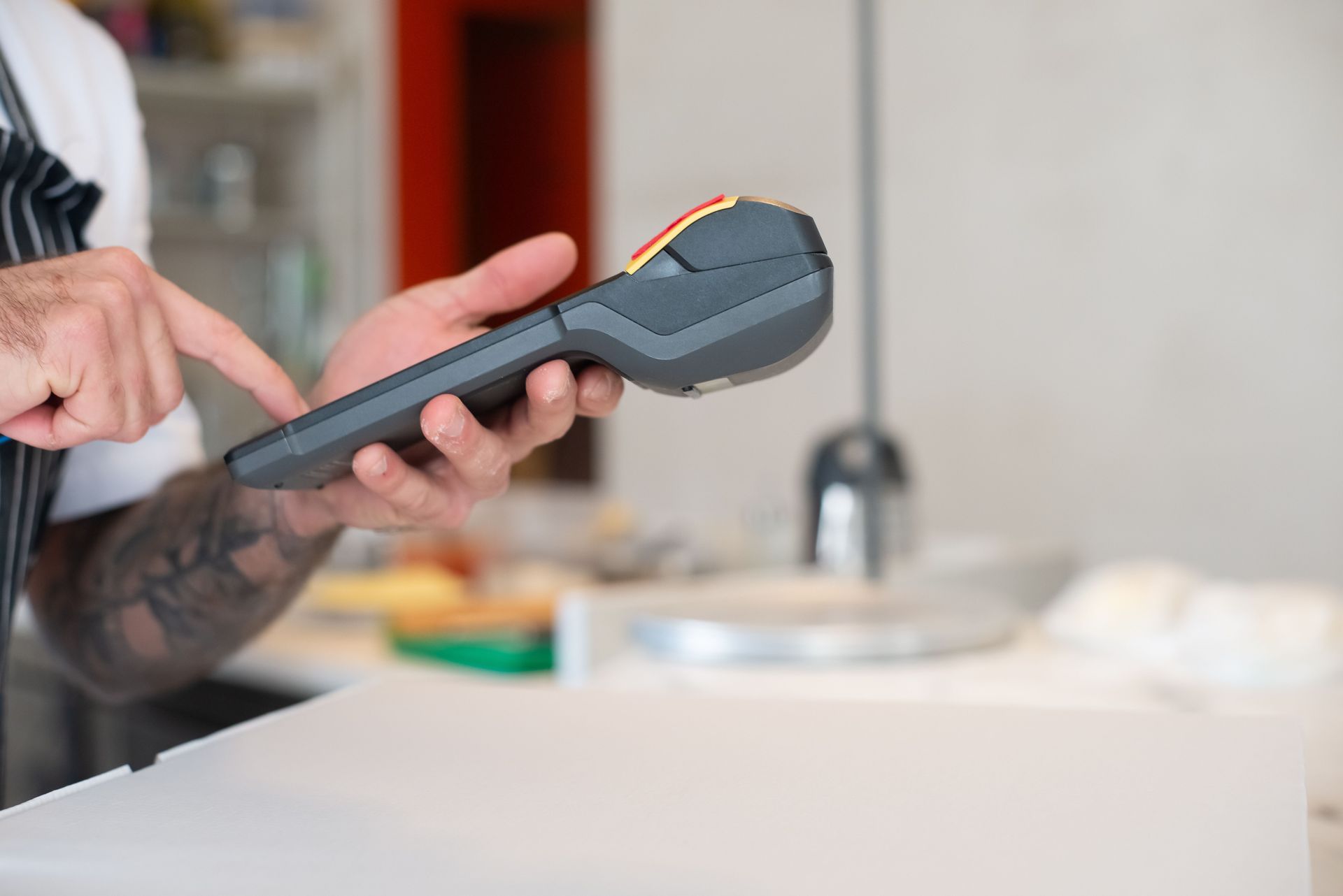 Hand holding a payment terminal during an in-person card payment at a restaurant counter for a local