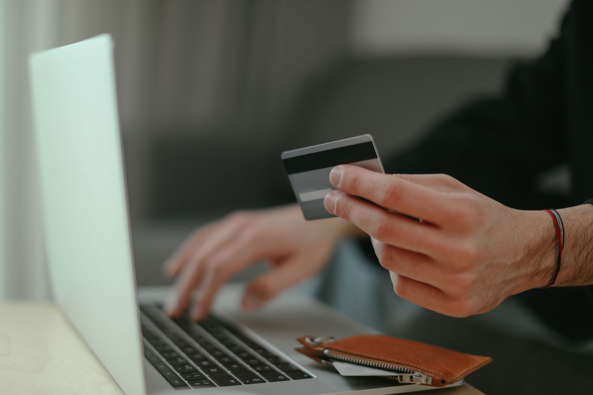 Hands holding a credit card near a laptop while typing, suggesting online shopping