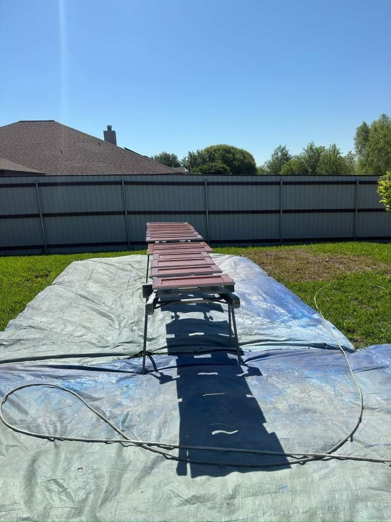 Fold-out chairs lined on a tarp in a backyard, with a hose and coiled wire in the foreground.