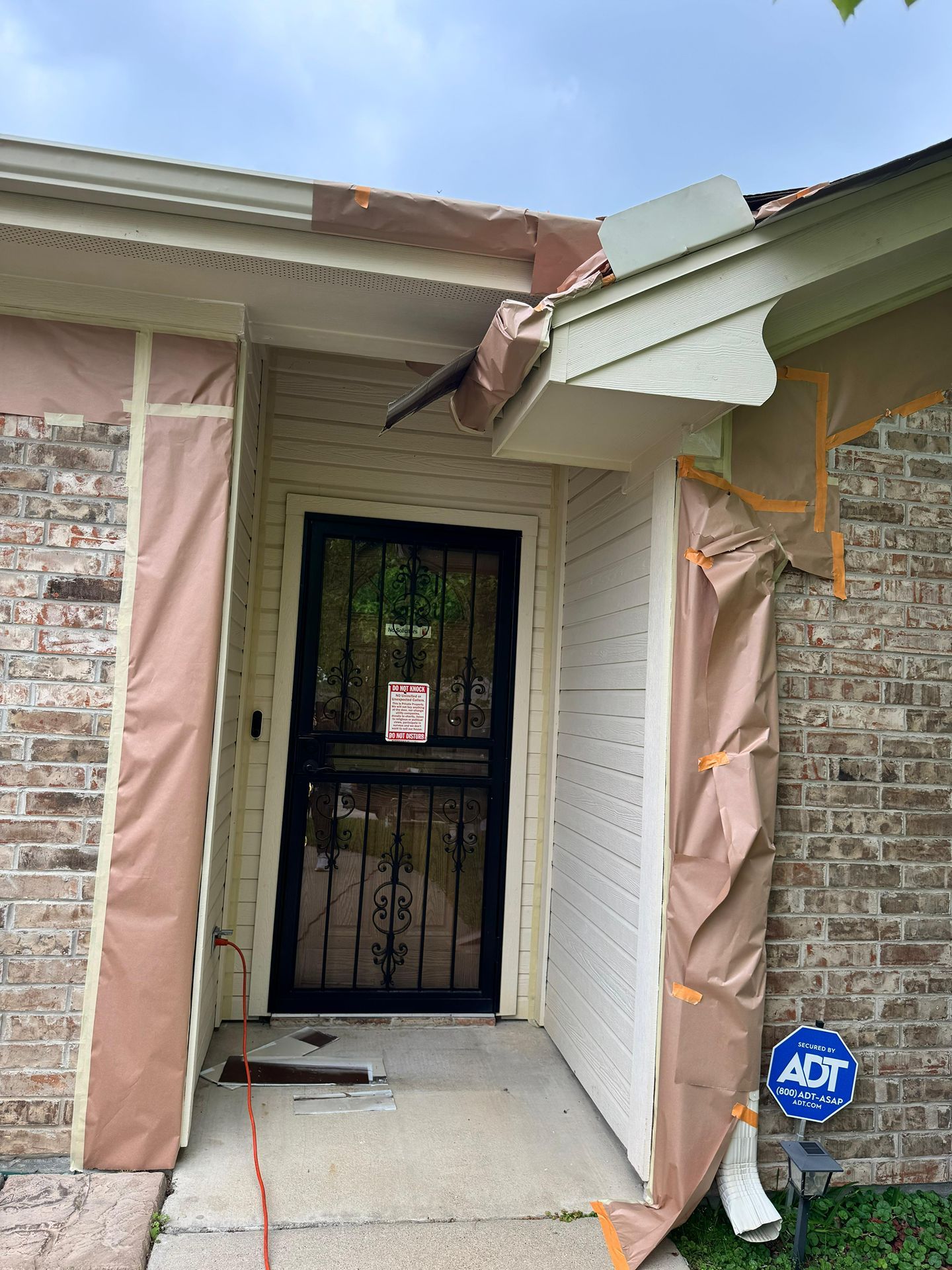 Damaged front entryway with torn siding, exposed insulation, and a black security door.