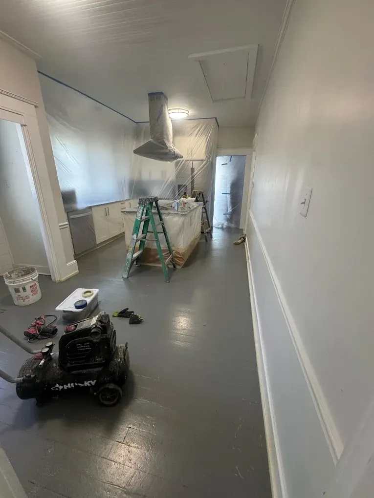 Indoor hallway under renovation with ladders, tools, and a work truck on the floor