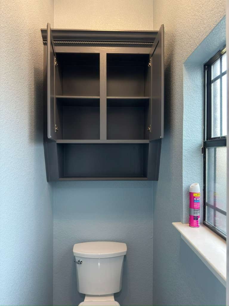 Small bathroom with an open dark wall cabinet above a toilet and a window ledge holding a can.
