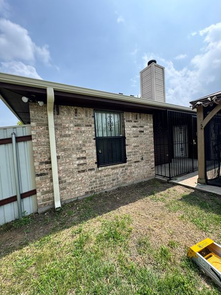 Brick house exterior with a small yard, front window, black gate, and cloudy sky.