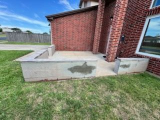 Concrete patio and steps beside a red brick house with a patch of grass in front.