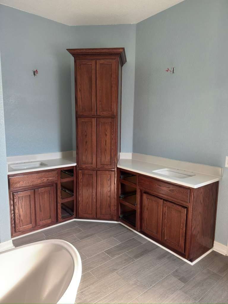 Corner bathroom vanity with white countertops, dark wood cabinets, and a tall central storage cabinet