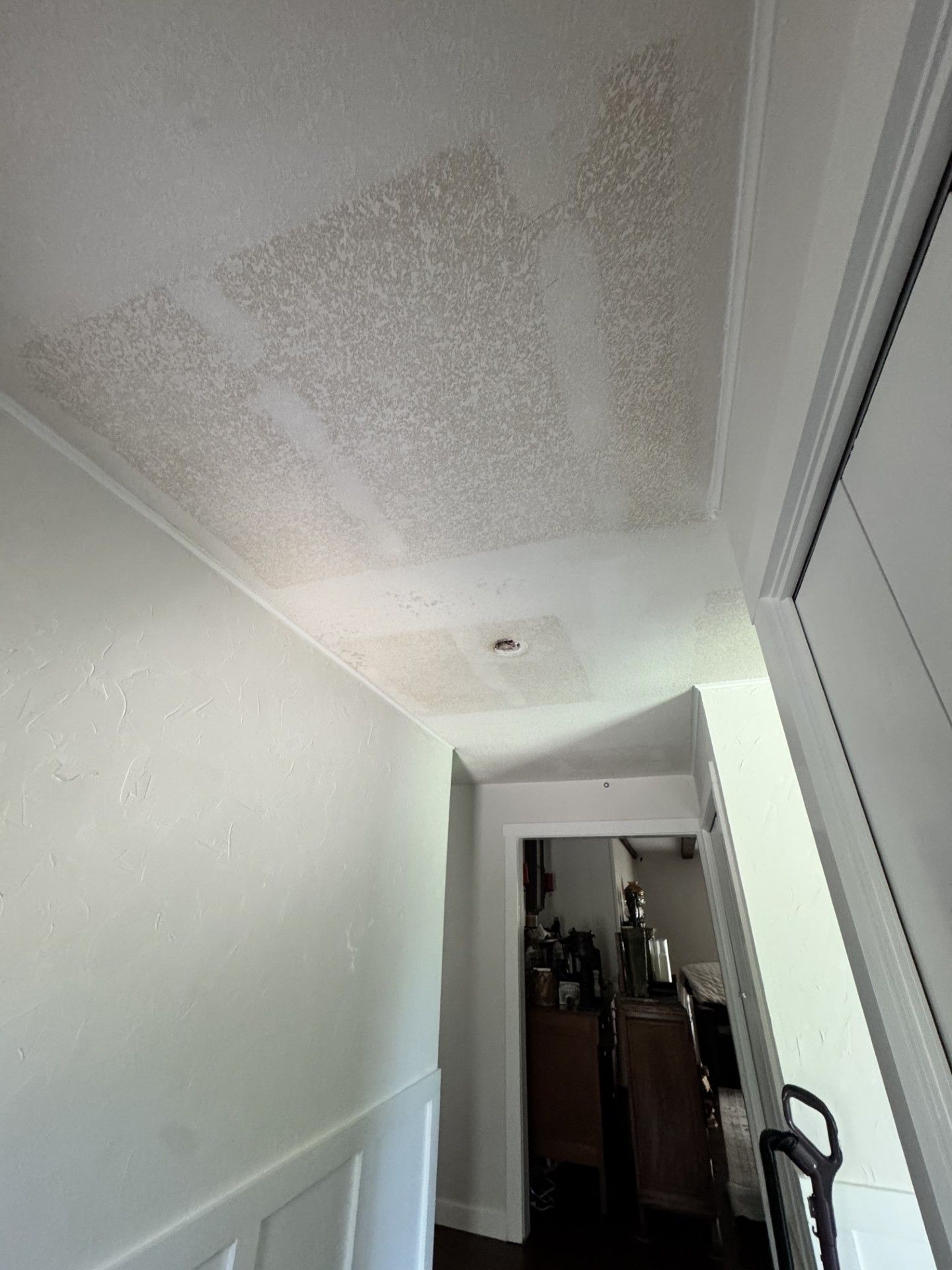 Hallway ceiling with water damage and peeling paint above white walls and doorways
