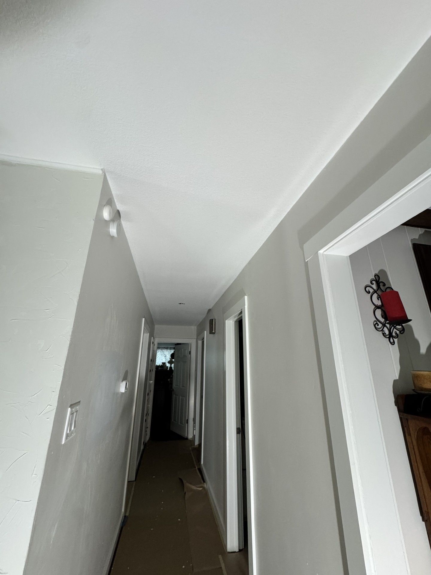 Narrow hallway with gray walls, white trim, and doors on both sides, lit by a ceiling bulb.