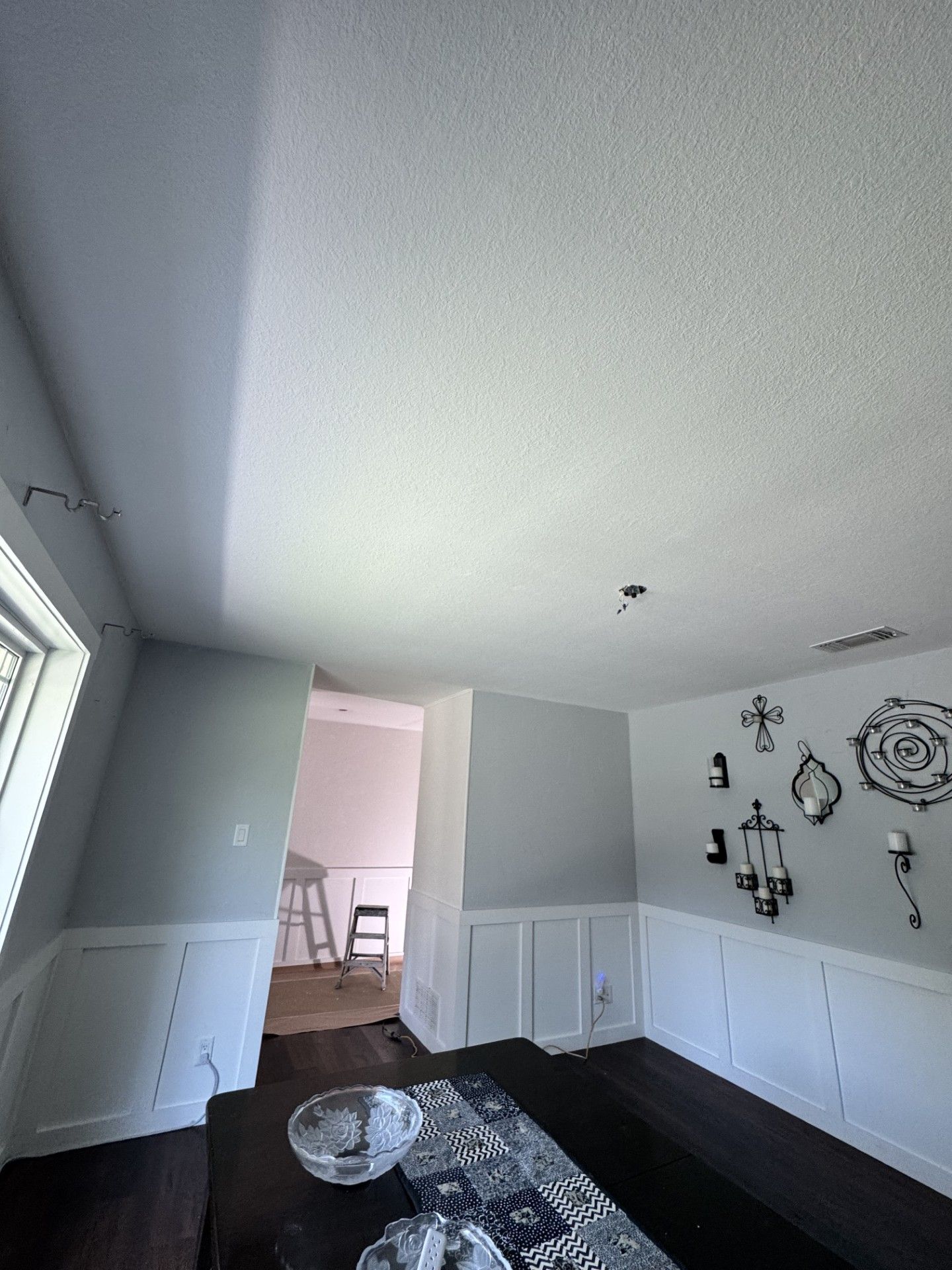 Gray dining room with black bench, white wainscoting, patterned rug, and wall decor, viewed toward a doorway