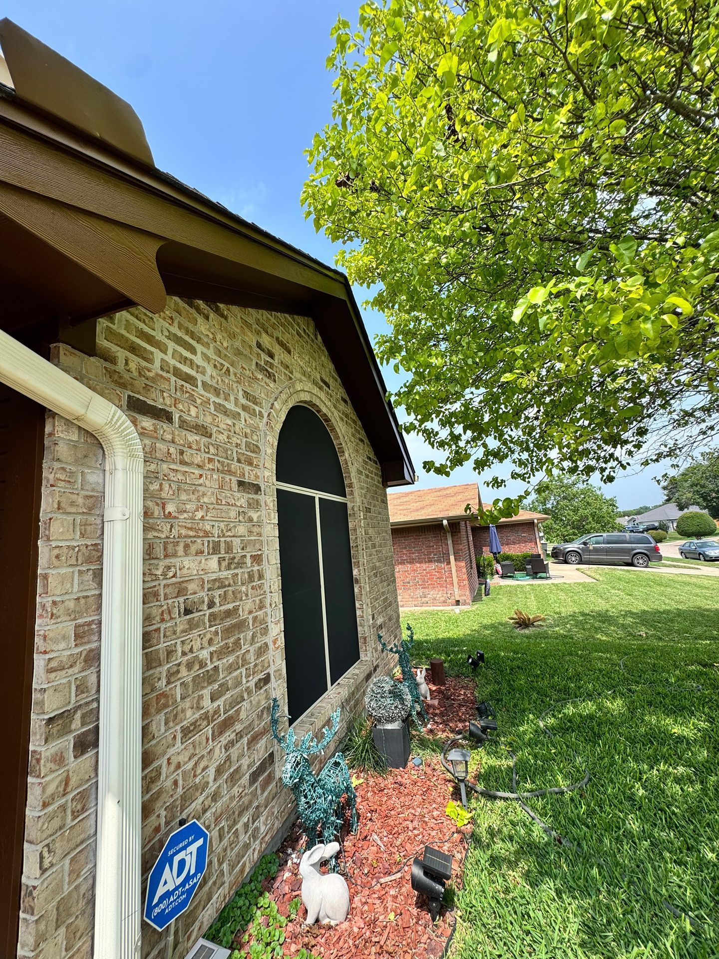 Brick house exterior with a black window screen, tree shade, and a landscaped front yard