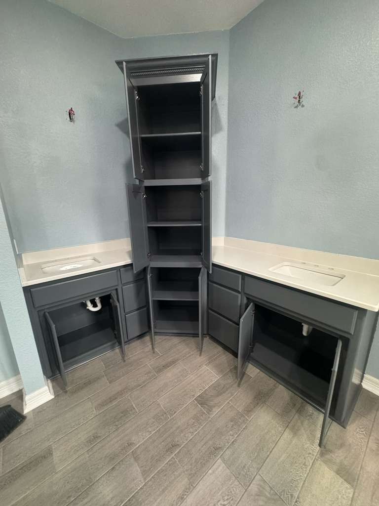 Small empty corner office with built-in dark shelves and gray desks against light walls