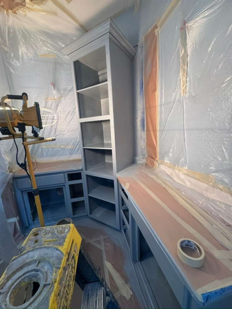 Masked kitchen under renovation with plastic sheeting, gray cabinets, and a painter’s tool on a countertop