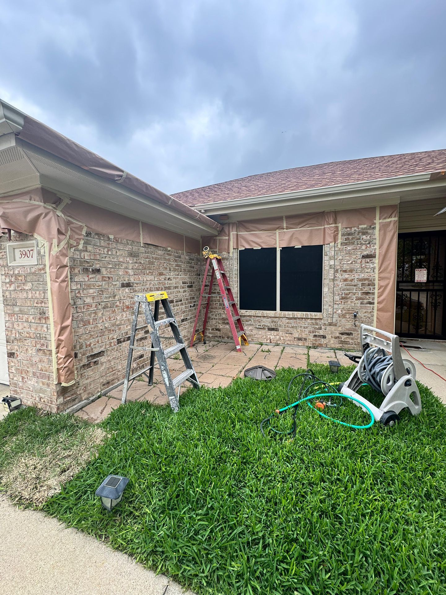 Two-story brick house exterior with ladders, tools, and a window under repair in the yard