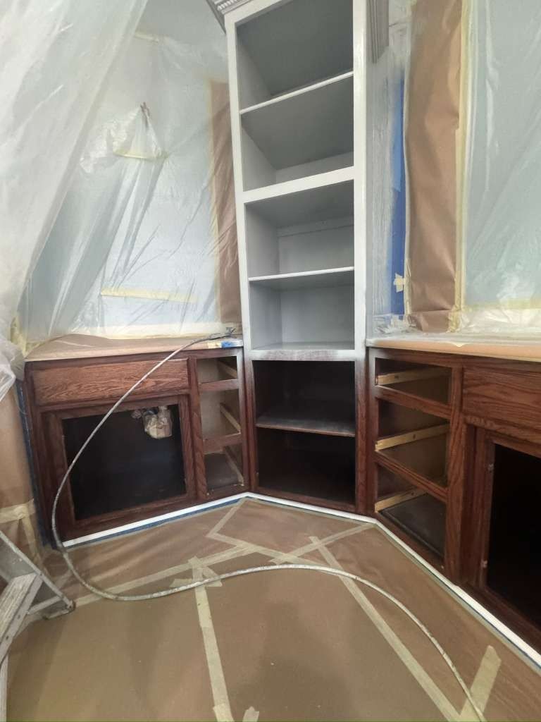 Kitchen cabinets under renovation, with plastic coverings and a white built-in shelf in the center.