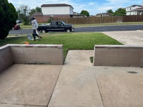 Front walkway with low concrete walls leading to a street, where a person walks past a black pickup truck.