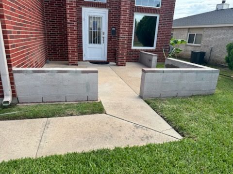 Brick house entrance with concrete walkway, raised planters, and a white front door
