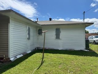 White-sided house exterior with a grassy yard, blue sky, and a clothesline pole in the center
