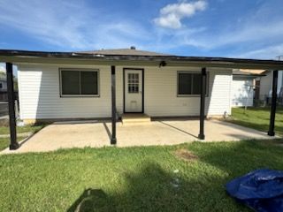 Single-story white house porch with black posts, front door, windows, and concrete patio under a blue sky