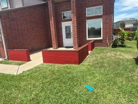 Brick house exterior with white door, red porch, and green lawn under bright daylight.