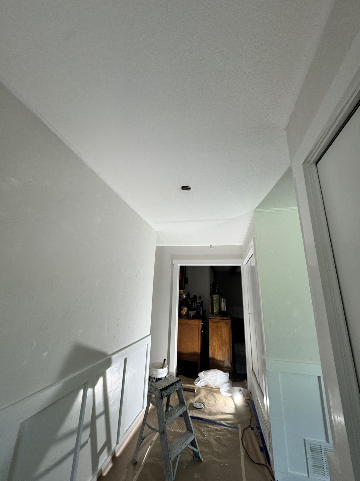 Narrow hallway with white walls, a chair, and renovation materials near an open doorway