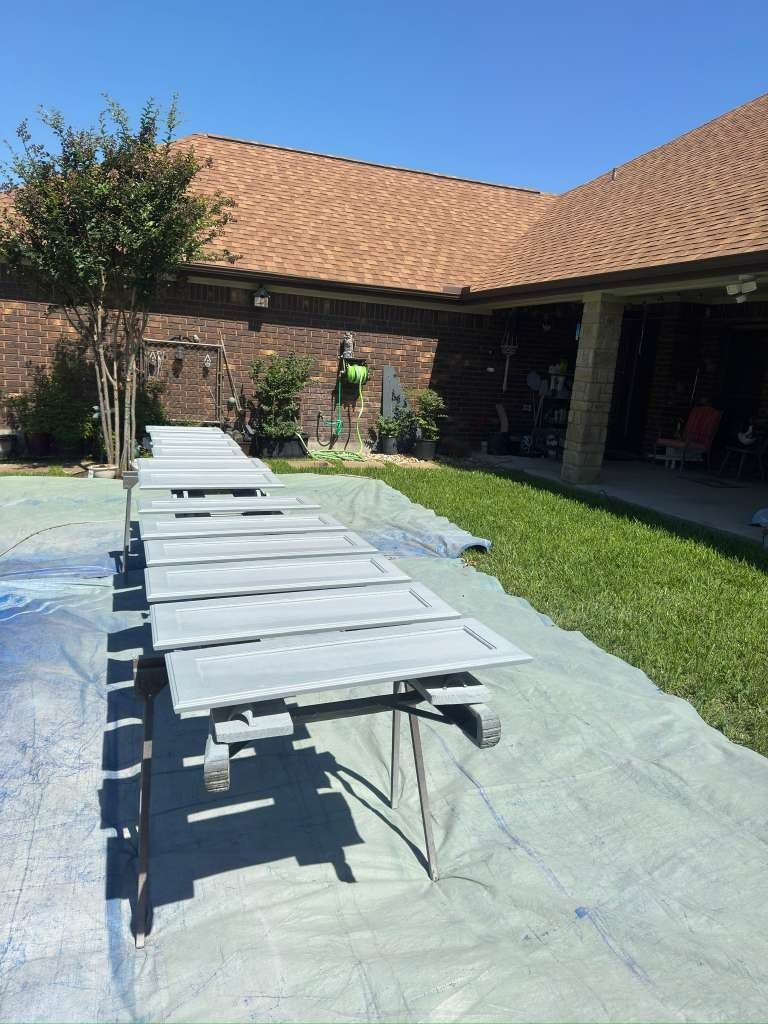 Folded picnic table on a tarp in a grassy courtyard beside a brick building with a red-tile roof.