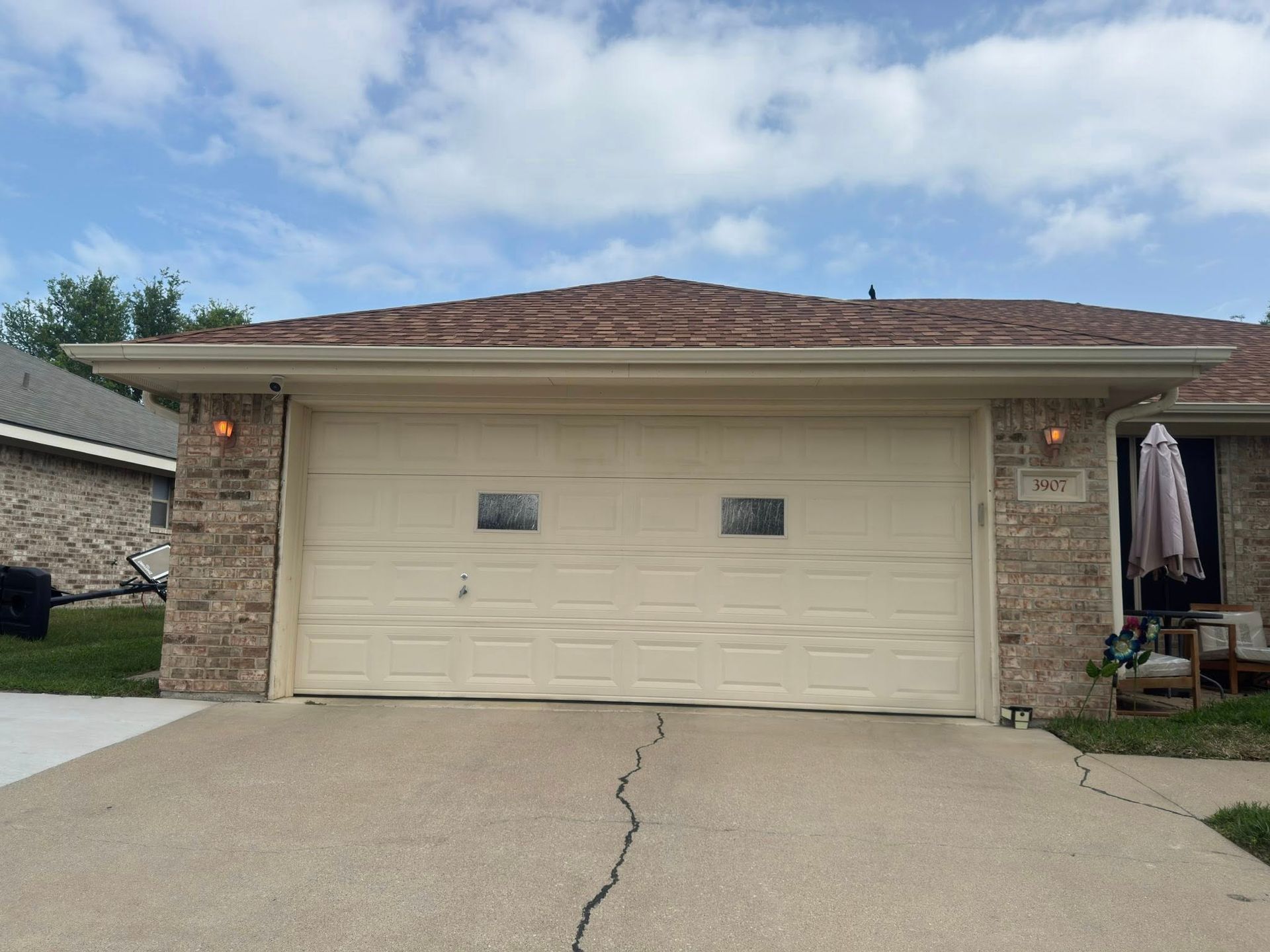 Suburban two-car garage with beige doors, stone accents, and a cracked concrete driveway under a cloudy sky