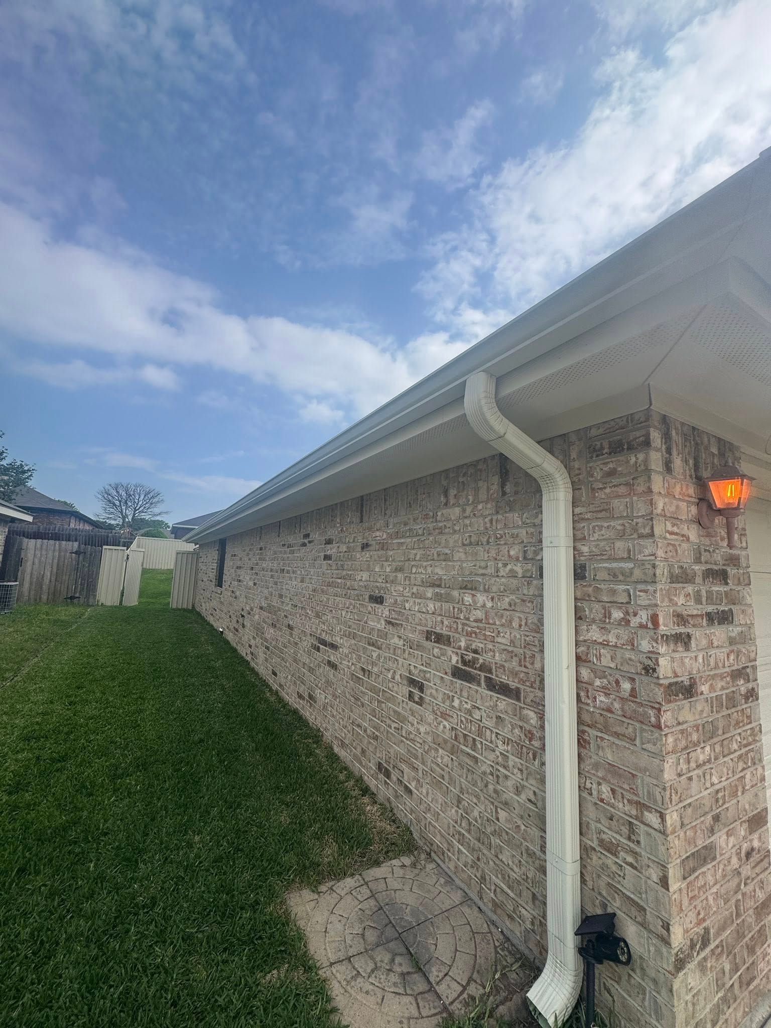 Brick house side with white gutter, green hedge, and cloudy sky overhead.