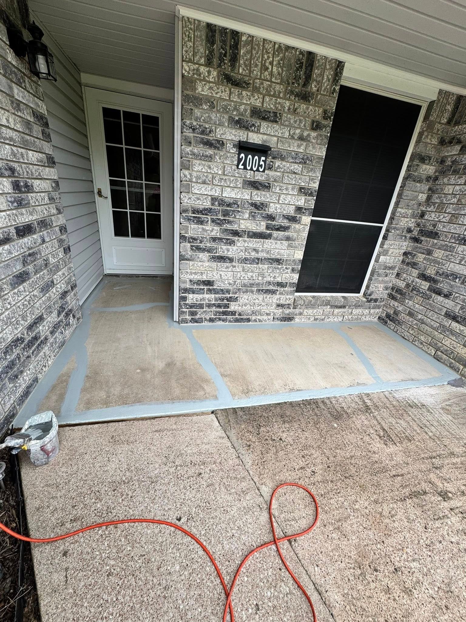 Front porch with white door, gray stone walls, and tan carpet; red cords lie on the floor.