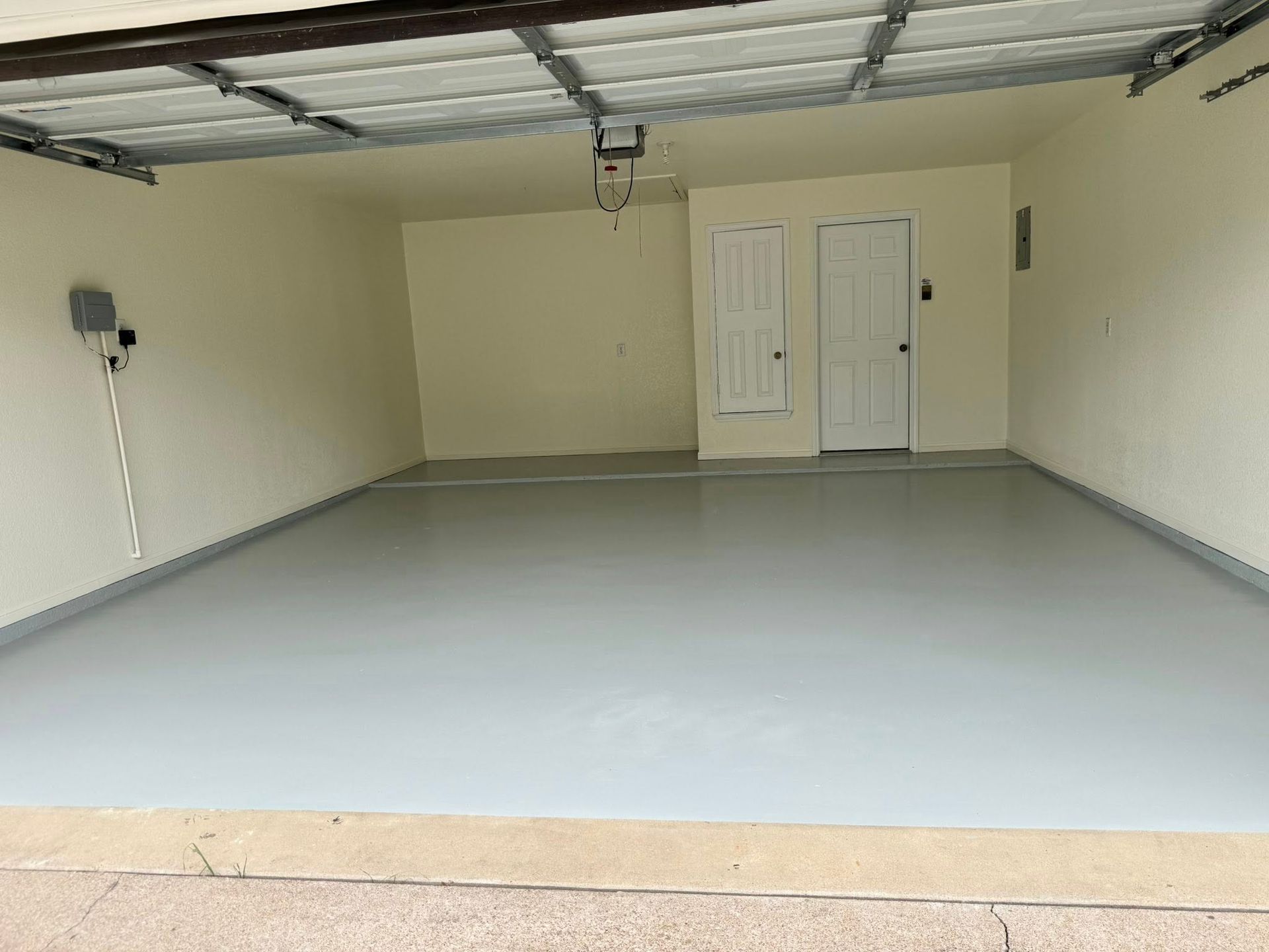 Empty two-car garage with a light gray floor, beige walls, and white doors at the back.