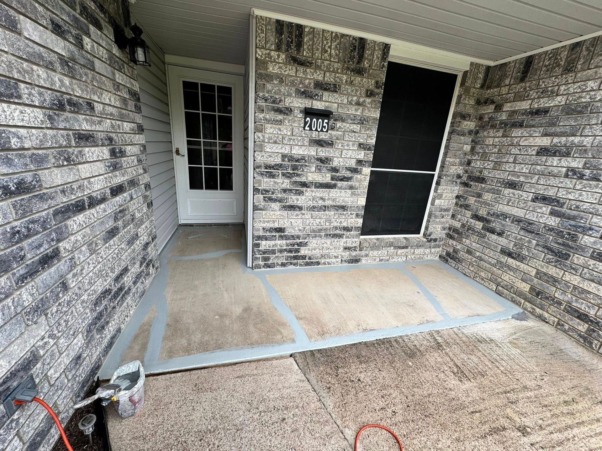 Covered front porch with brick walls, concrete floor, white door, and a black security screen door.