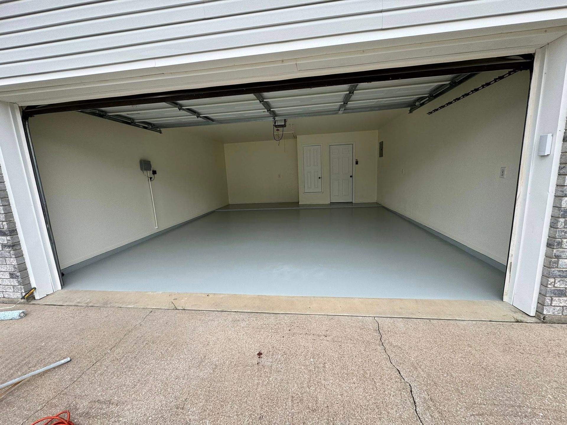 Empty two-car garage with open door, white walls, gray floor, and a side door at the back.