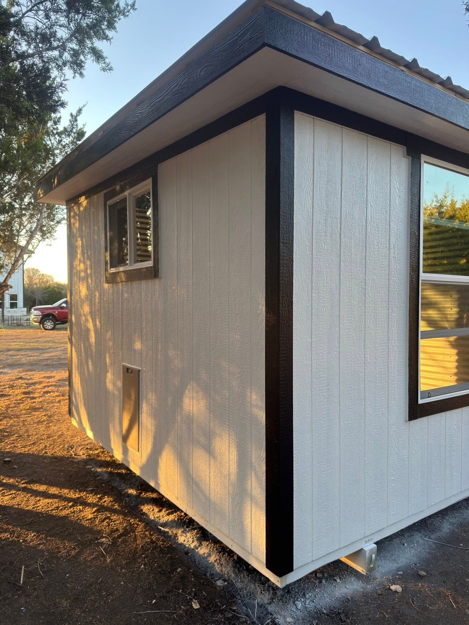 Small white building with black trim and a sloped roof, viewed from the corner outdoors.
