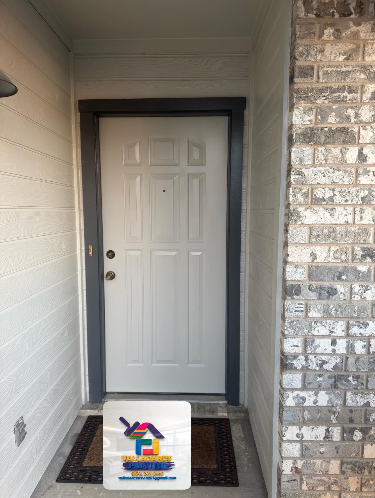 Front porch with a white front door, brick wall, doormat, and a small sign on the floor.