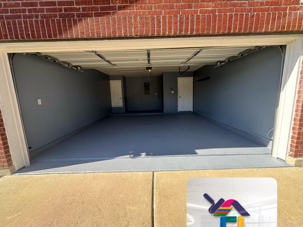 Empty two-car garage with open door, gray floor, and brick exterior.