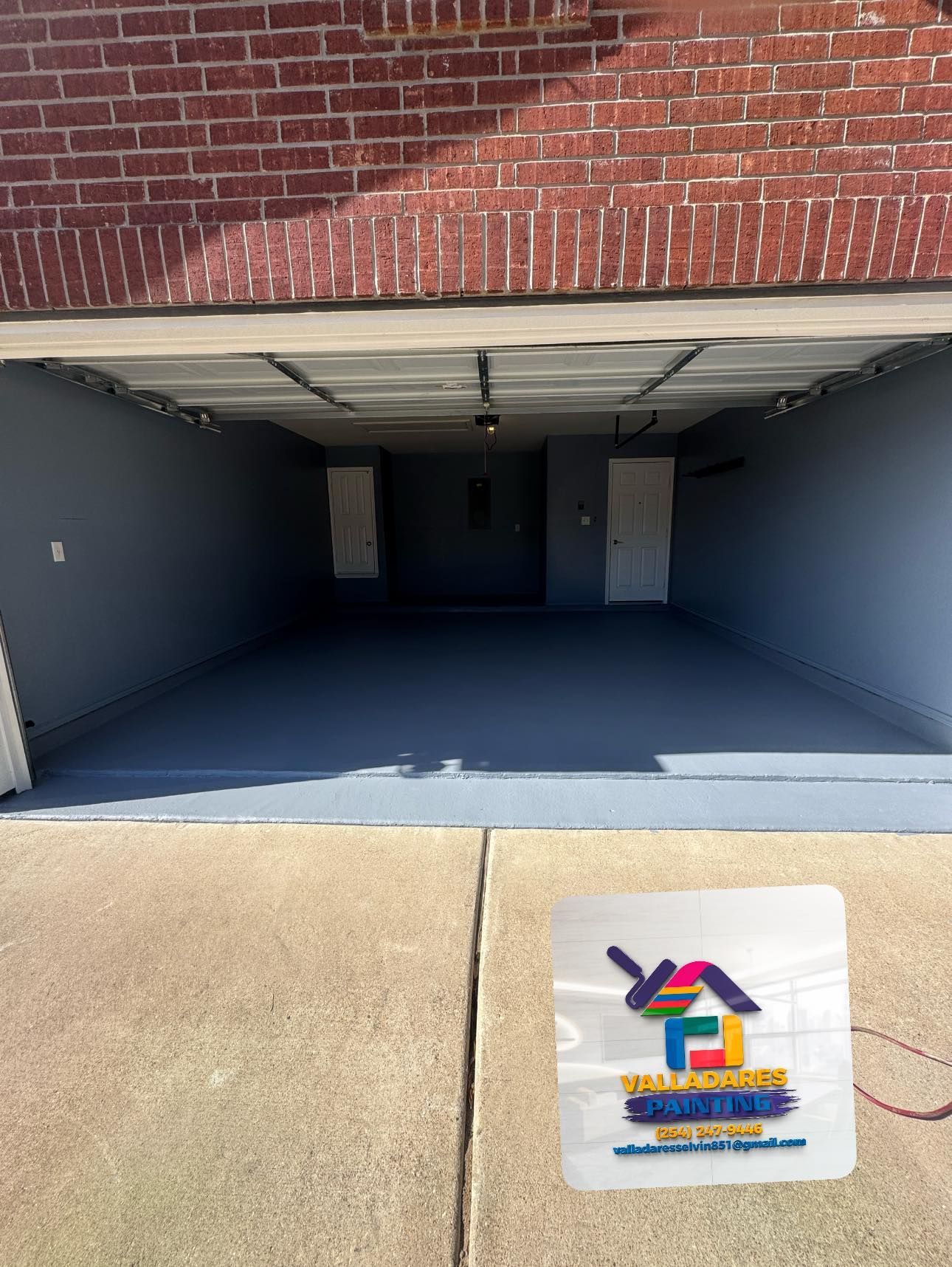 Empty garage under a brick building with a concrete floor and a sign on the ground in front.