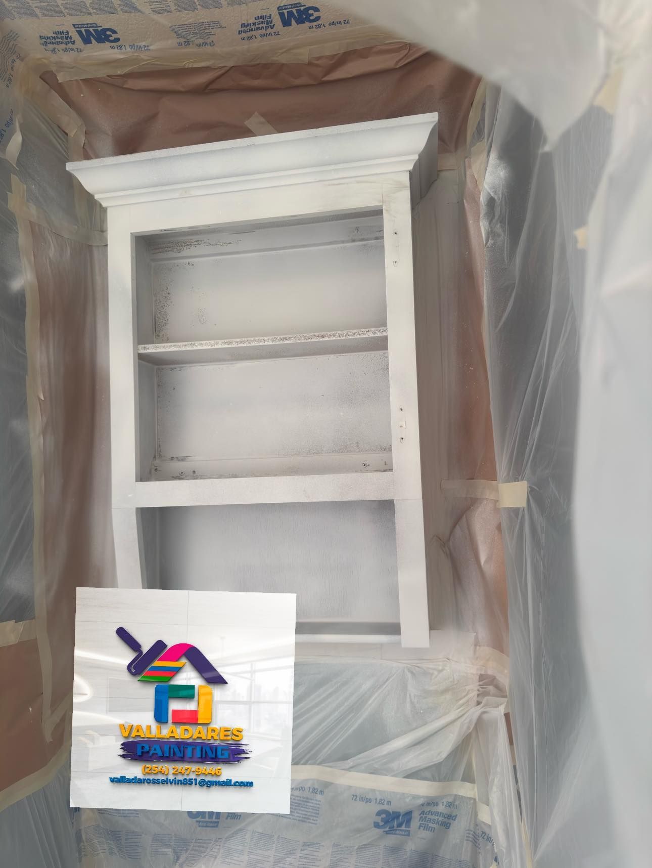White wooden cabinet or shelf unit wrapped in plastic, with a sign taped near the bottom.