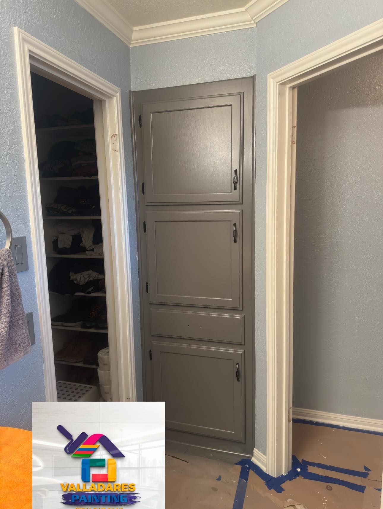 Hallway with gray walls, a closed gray door, two open doorways, and blue painter’s tape on the floor.
