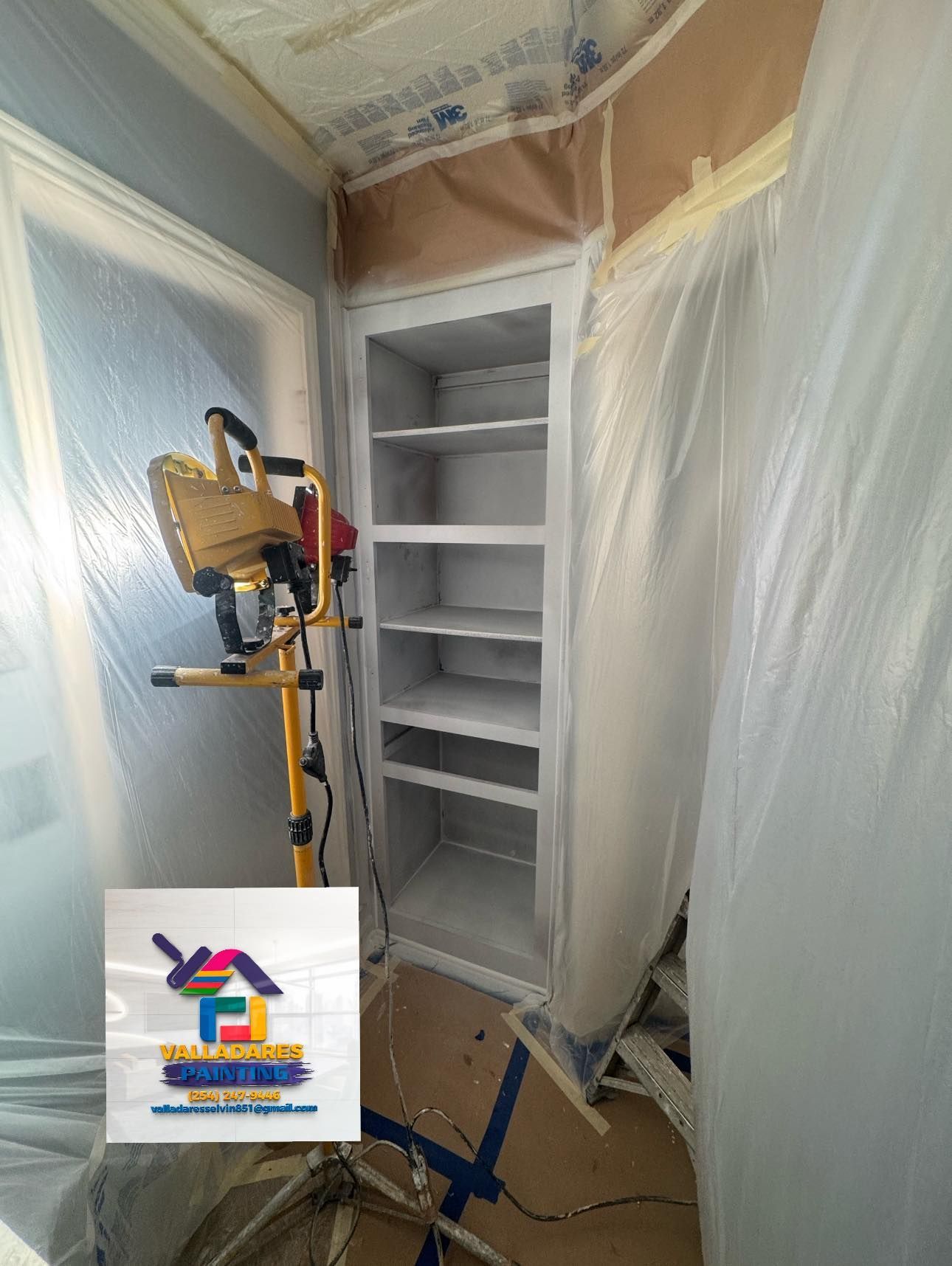 Paint sprayer painting a white built-in cabinet in a room masked with plastic sheeting