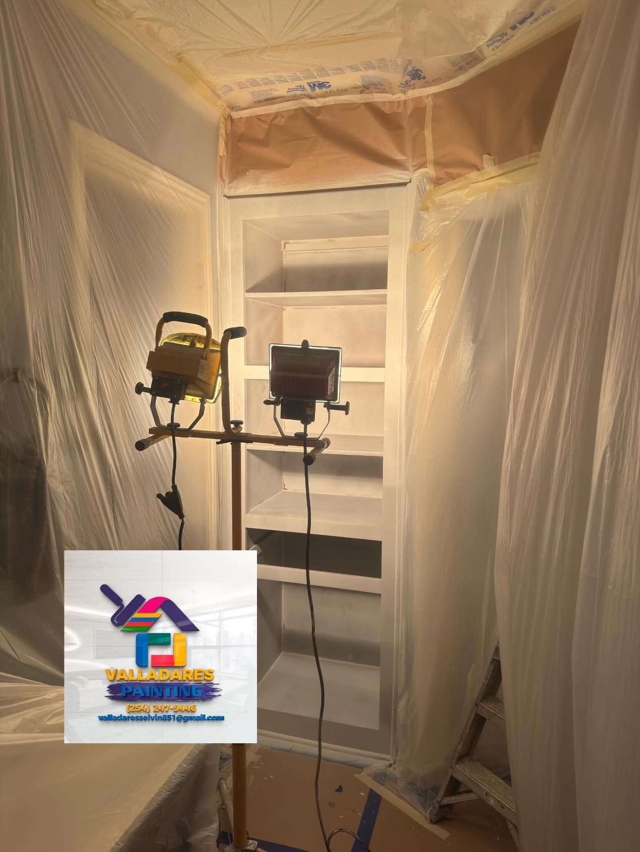 Two work lights on stands inside a plastic-sheeted room under renovation