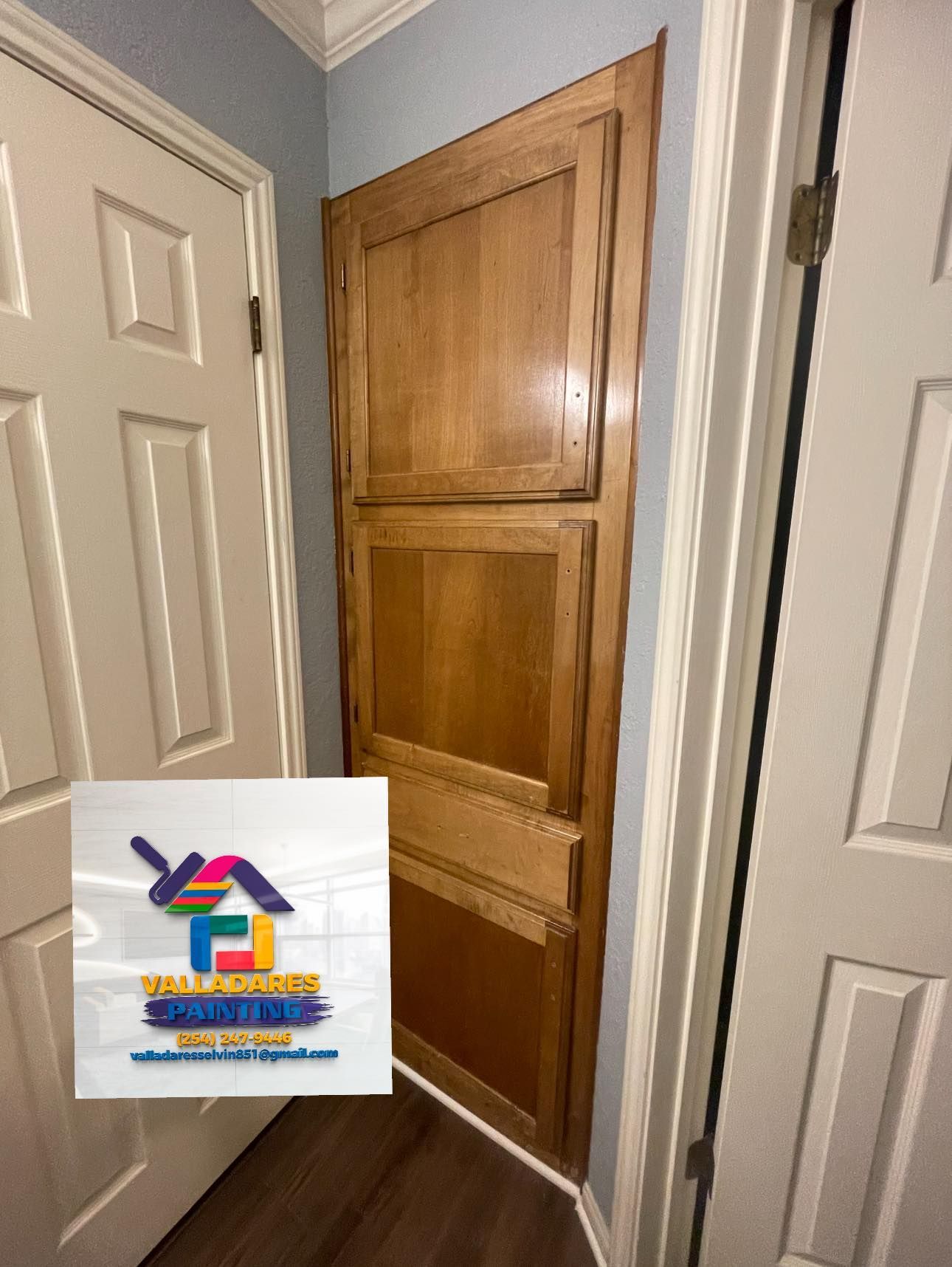 Narrow hallway with a wooden cabinet door between white doors and blue-gray walls