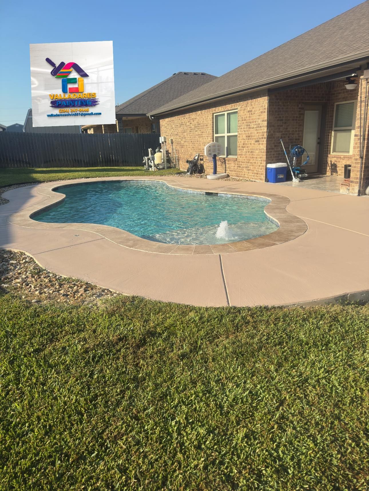 Backyard swimming pool beside a brick house, with a logo sign in the upper left corner.