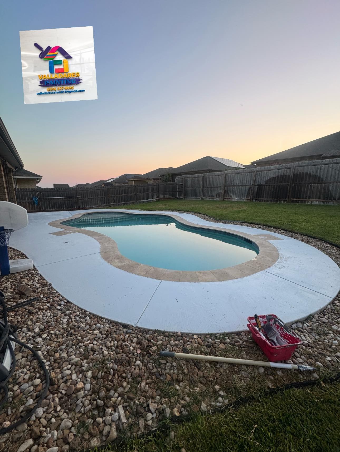 Backyard pool under construction at dusk, with gravel, white decking, and a red shovel in the foreground