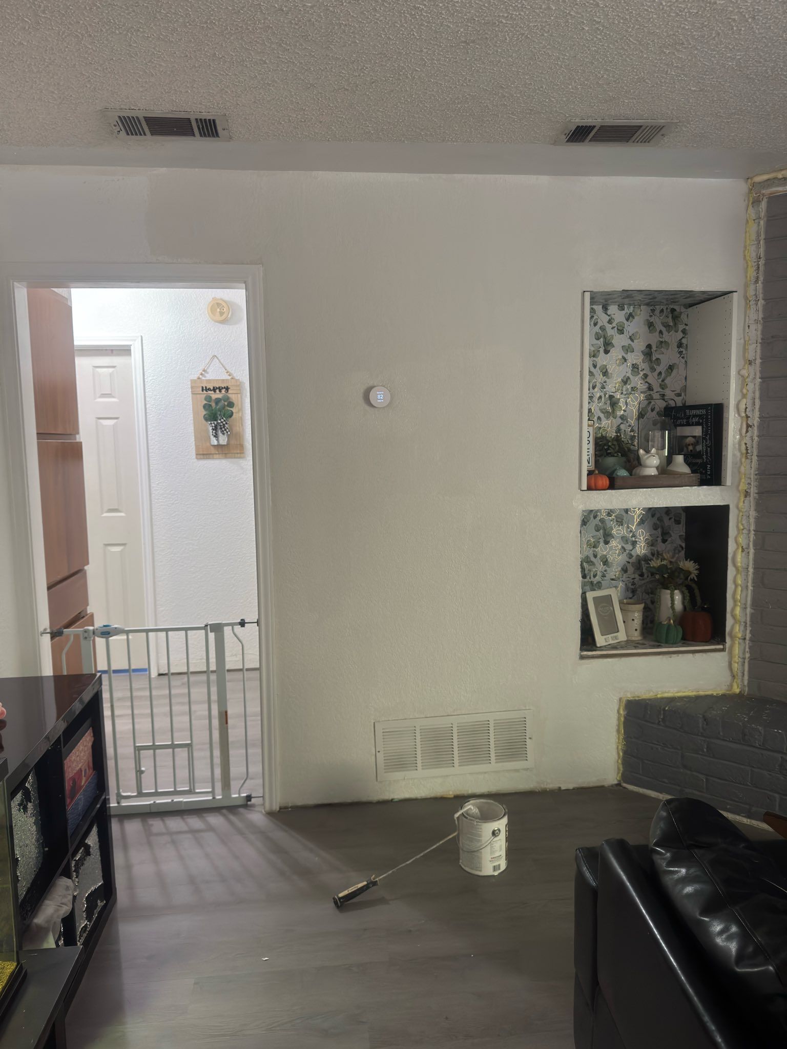 Living room with gray walls, black sofa, open doorway, wall niche shelves, and a paint can on the floor
