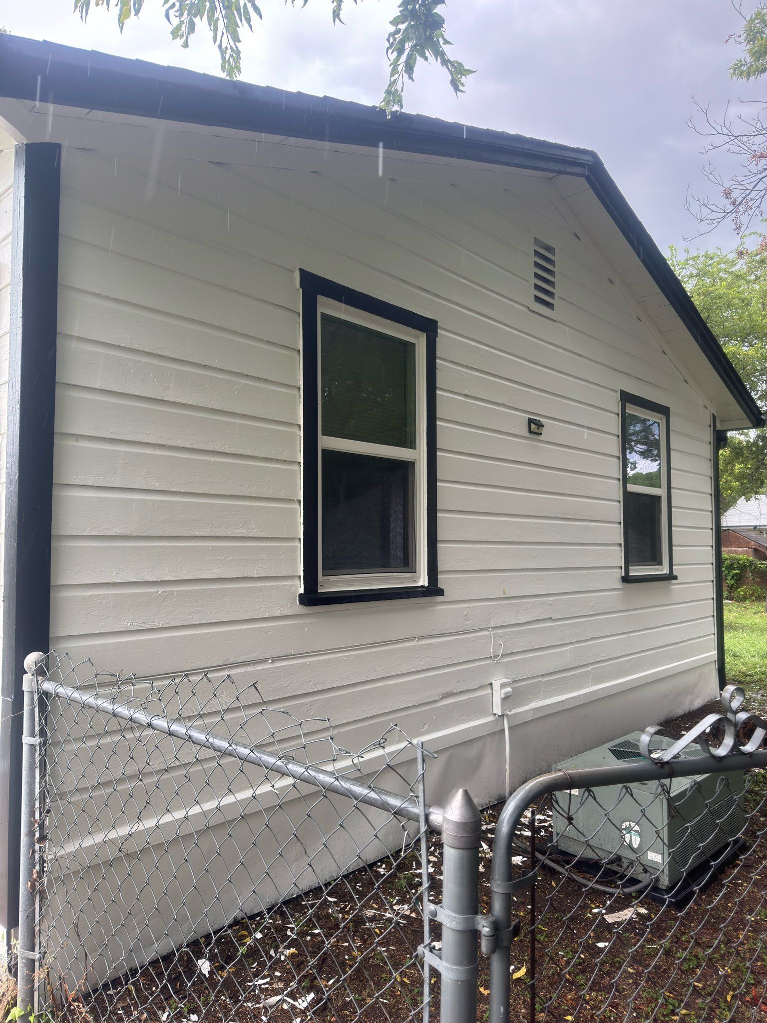 Side view of a beige house with black-trimmed windows and a chain-link fence in front