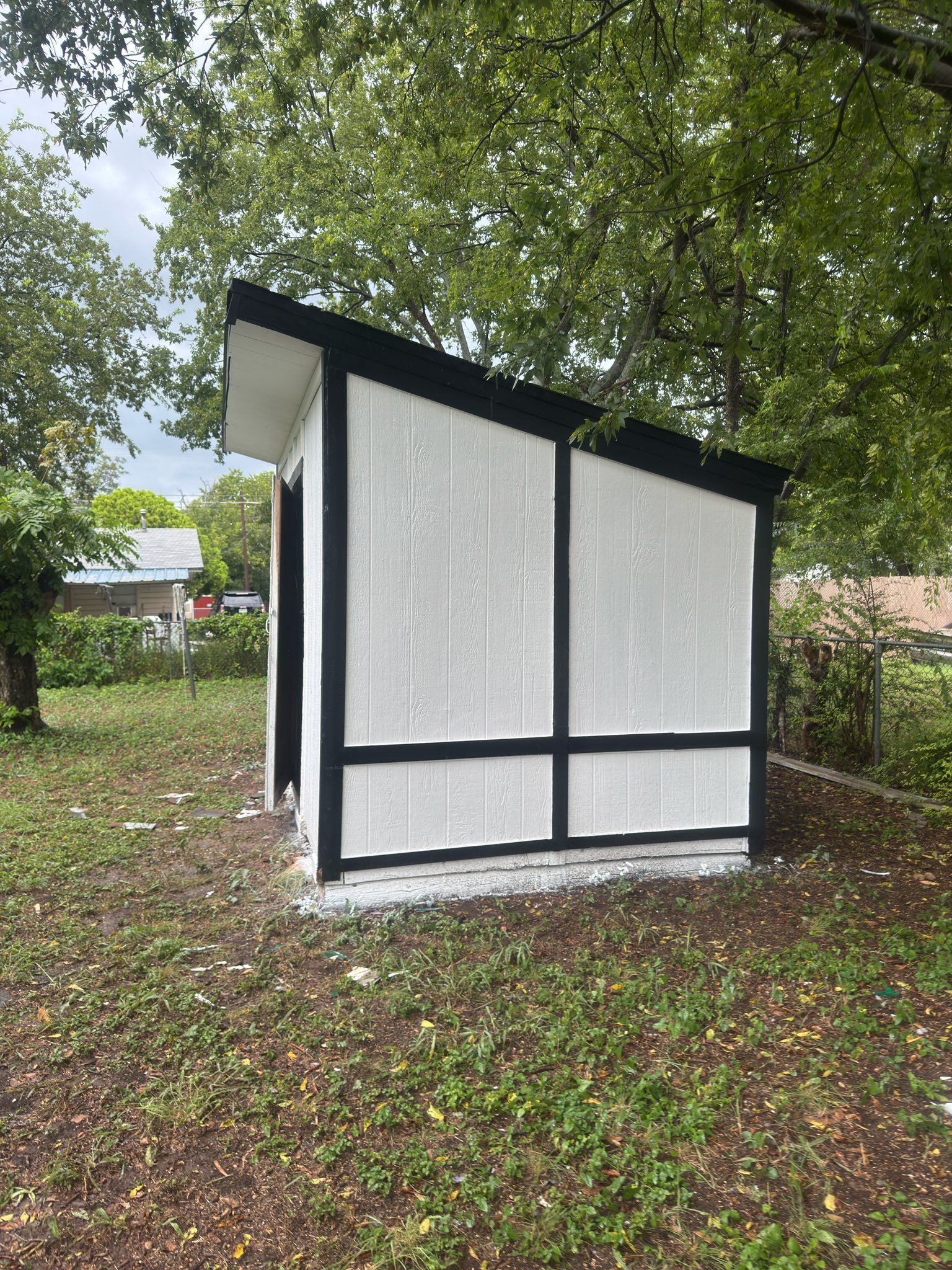 Small white and black outdoor structure with slanted roof under trees on grass
