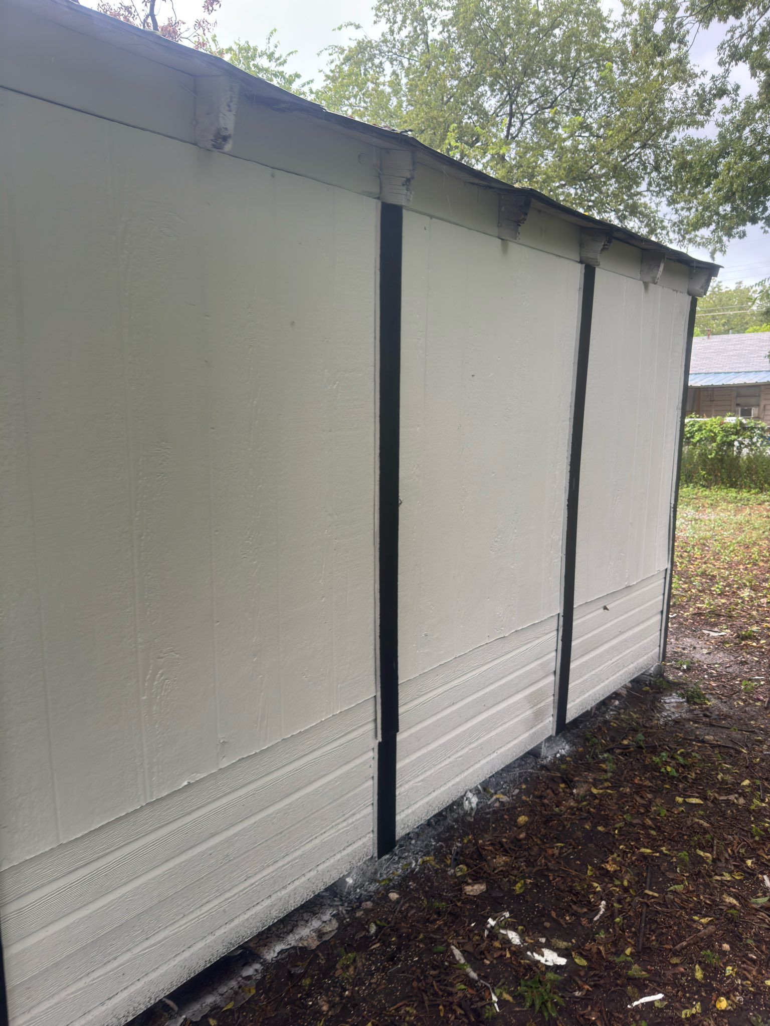 White shed wall with black trim and a slanted roof in a grassy yard.