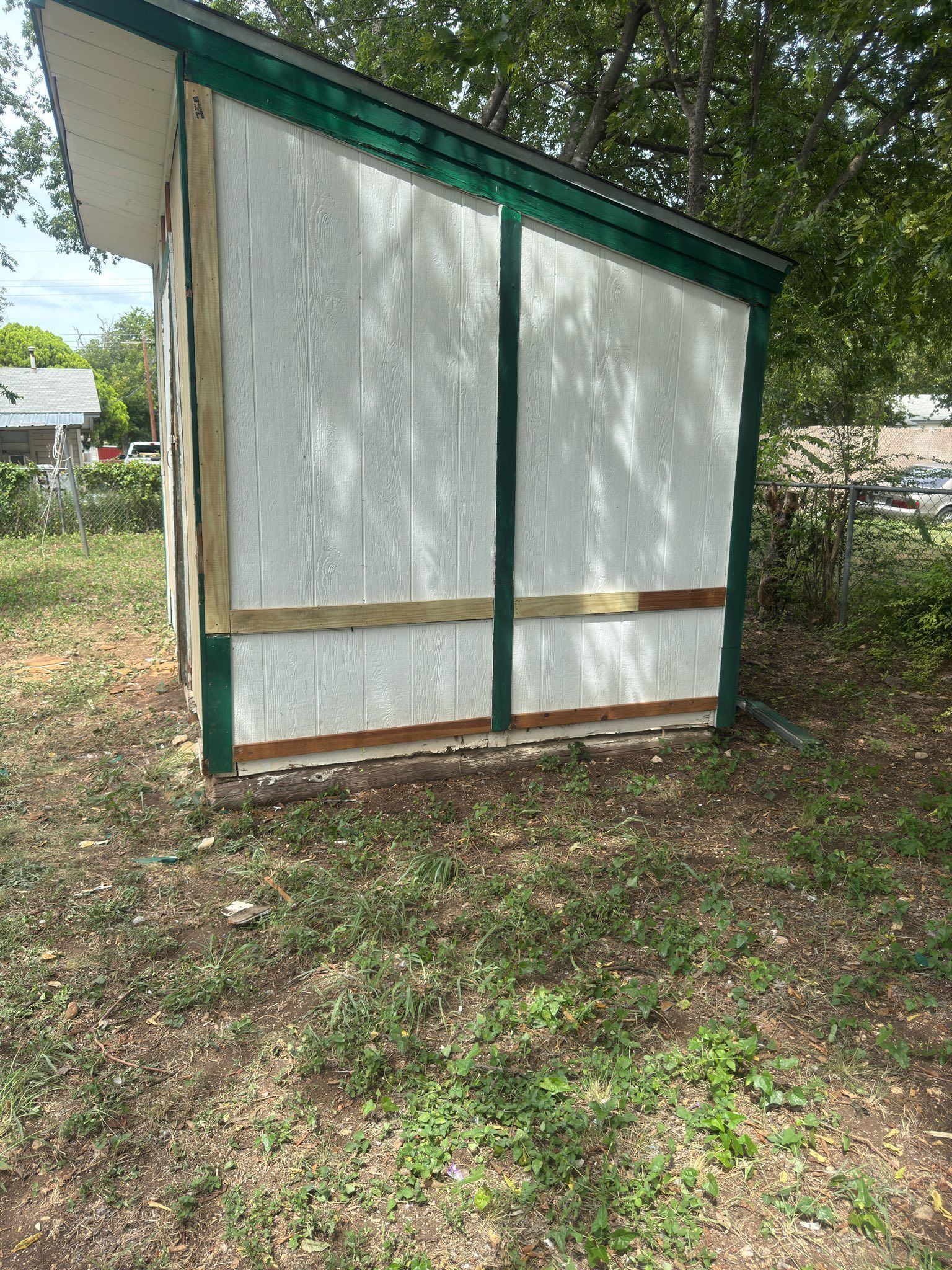 Small white shed with green trim in a grassy yard, viewed from the side.