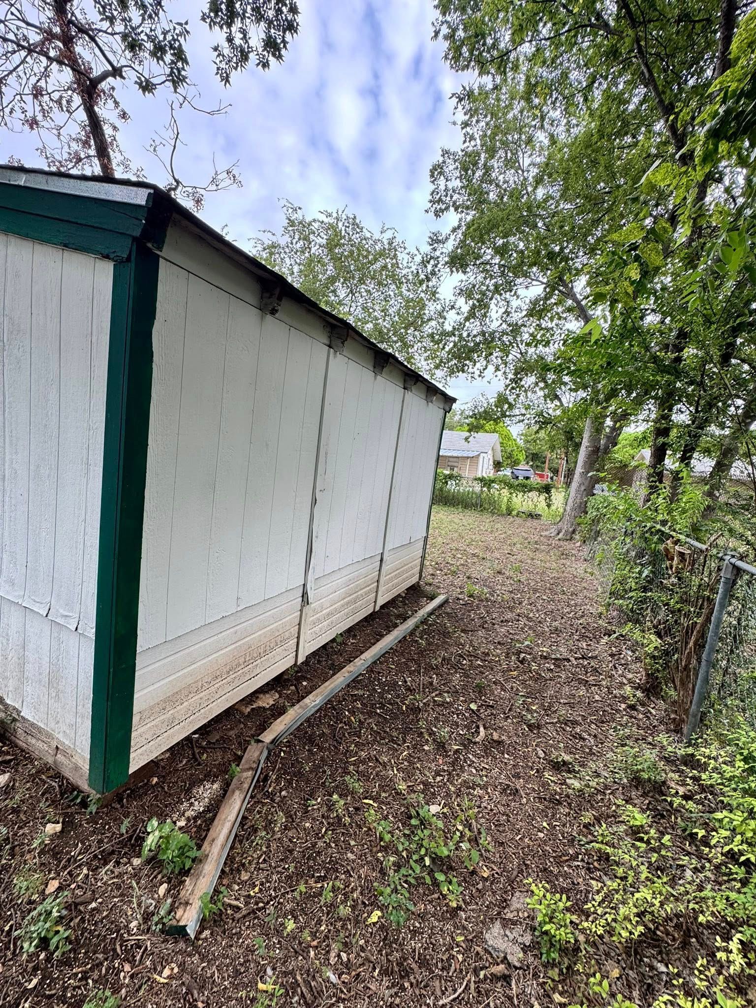 Small white shed with green trim beside a leafy yard and fence path