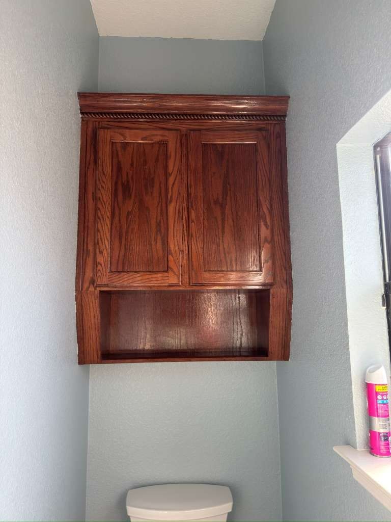 Small bathroom alcove with a wooden cabinet above a toilet and a window ledge on the right.